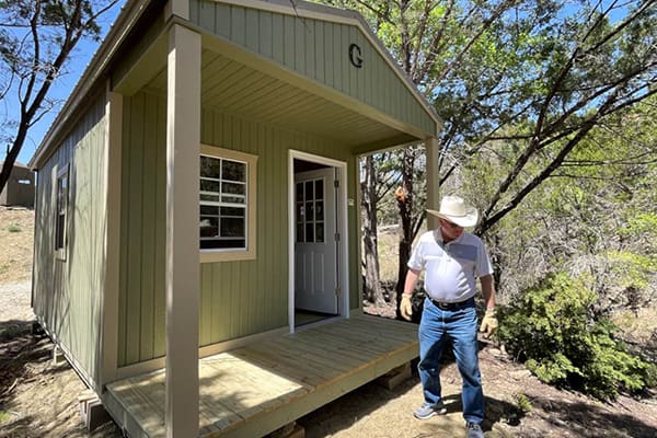 A man standing in front of a small cabin.
