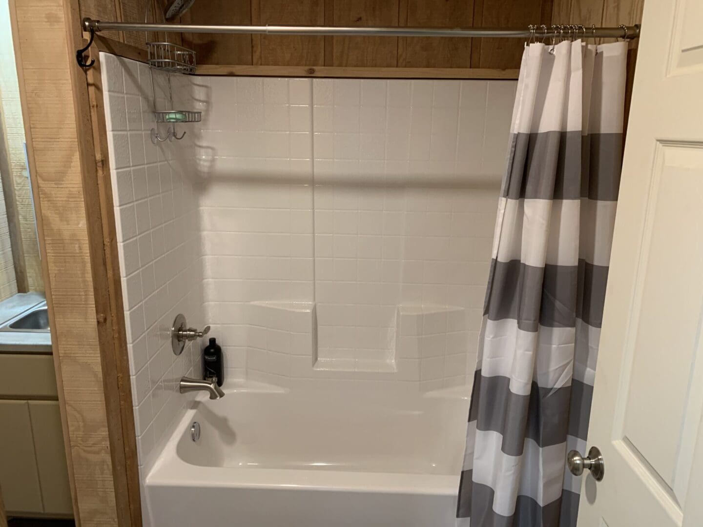 A view of the white tiled bath tub with the curtain