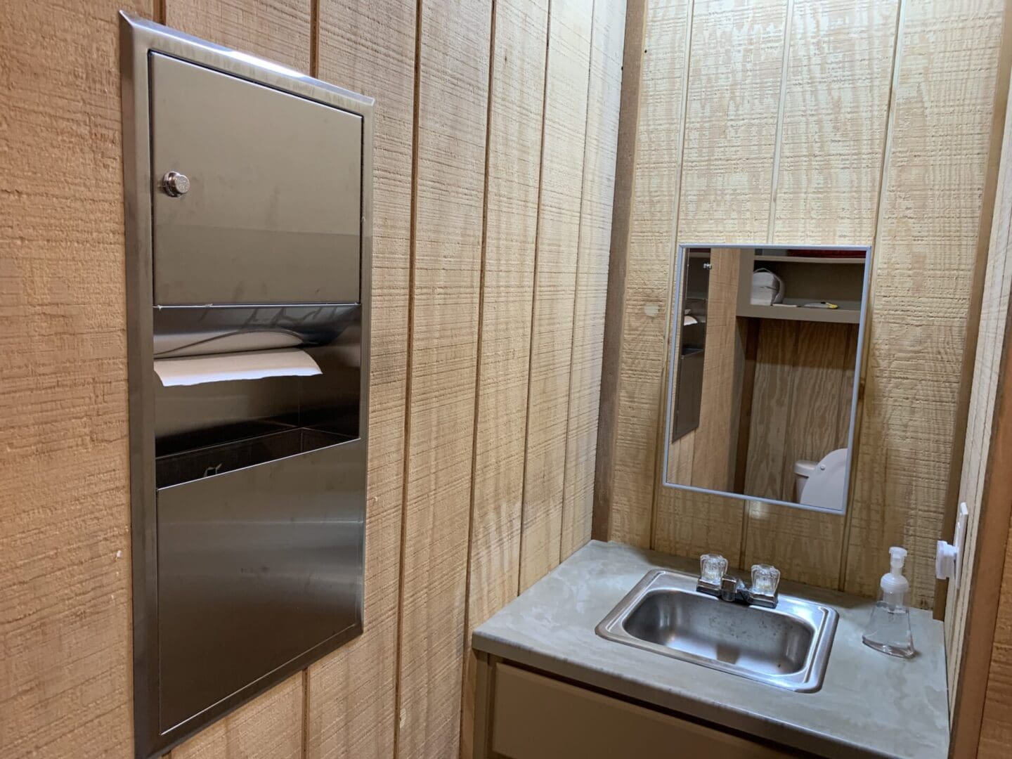 A bathroom with wood paneling and stainless steel sink.