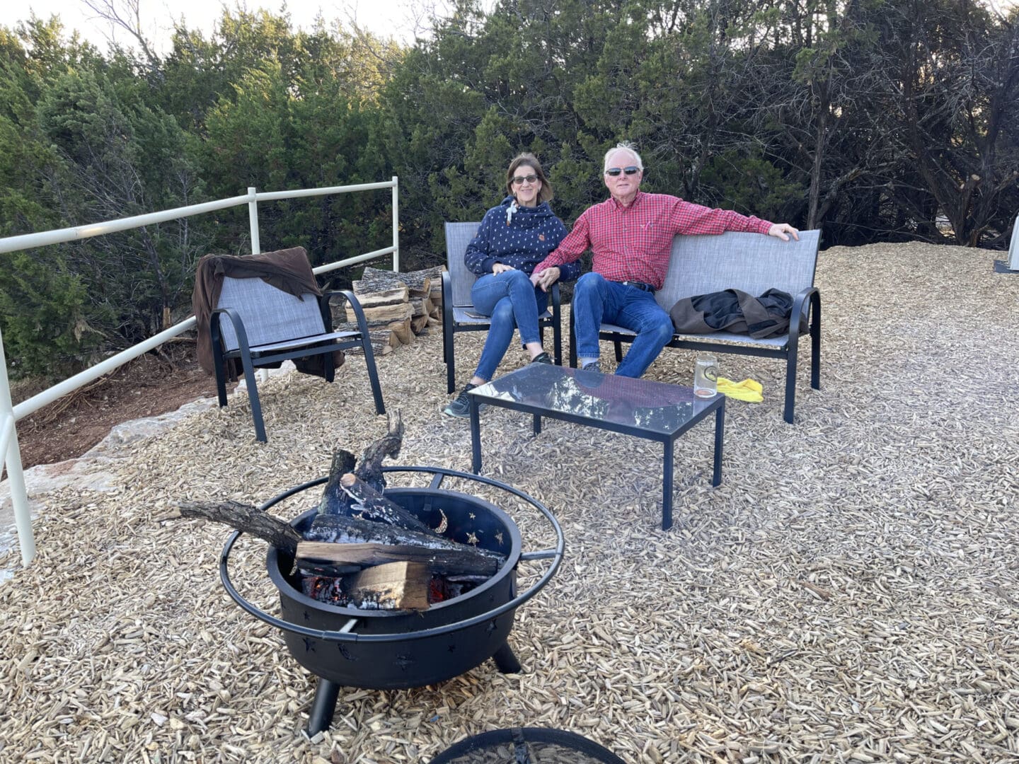 Two people sitting on a bench in front of an outdoor fire pit.