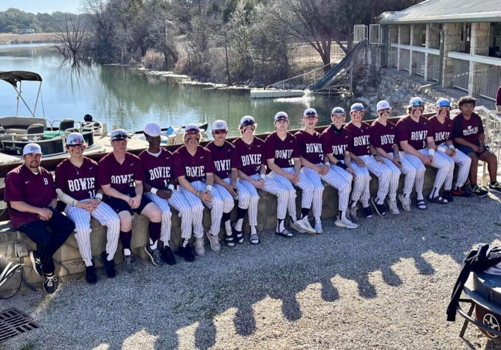 A baseball team is posing for a picture near a lake.